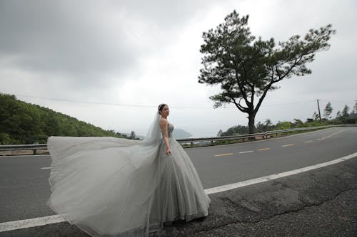 Photo of a Bride in a Gray Wedding Gown Standing on the Side of the Road