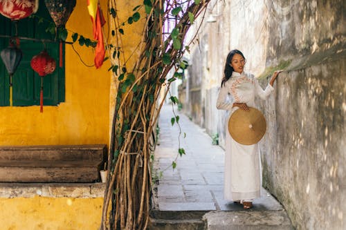 Free Woman in White Dress with a Conical Hat Standing on an Alley Stock Photo