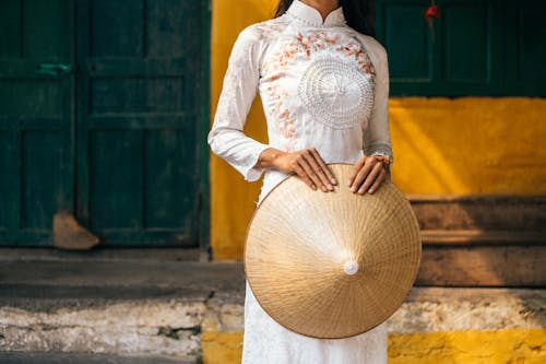 Person in White Dress Holding a Conical Hat