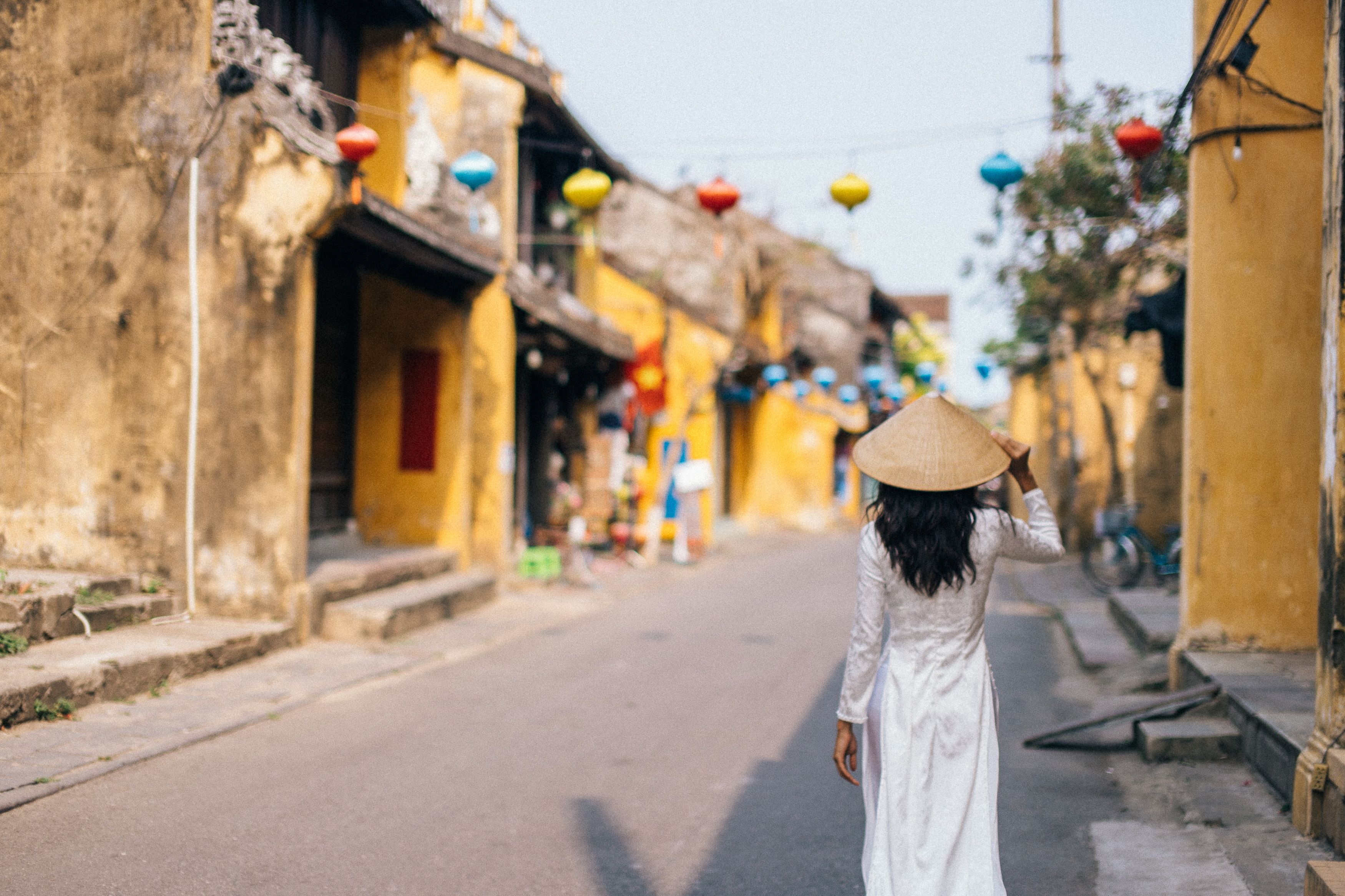 Back view of woman in ao dai and conical hat walking in Hoi An's vibrant streets. Back view of woman in ao dai and conical hat walking in Hoi An's vibrant streets.