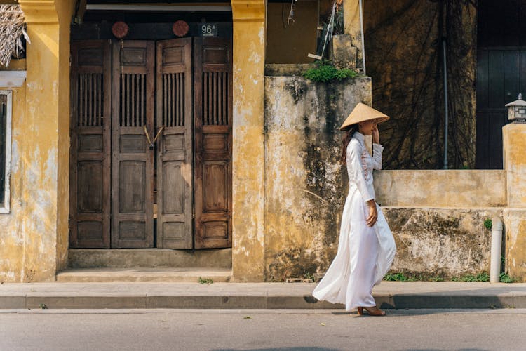 A Side View Of A Woman In White Dress Walking On The Street