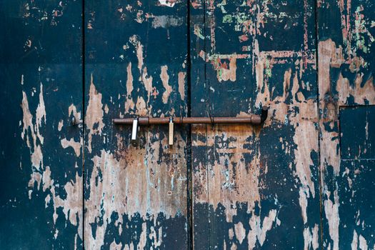 Close-up of a rustic, weathered door with peeling paint and iron latch.