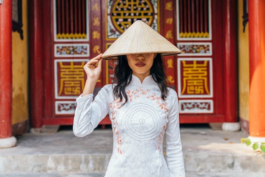 A woman wearing a traditional Ao Dai poses in front of a Vietnamese temple, showcasing cultural heritage.