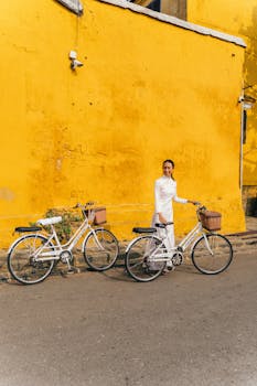 Vietnamese woman in traditional dress with bicycles in Hoi An, Vietnam against a yellow wall.