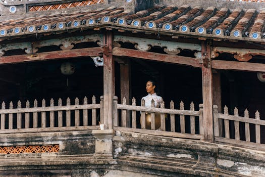 A woman in a traditional Vietnamese Ao Dai stands gracefully on an ancient building's balcony in Hoi An.