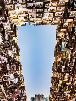 Upward perspective of densely packed urban apartments framing a blue sky.