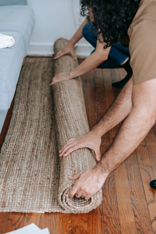 Free Couple rolling up a beige carpet on wooden floor, preparing for moving day. Stock Photo