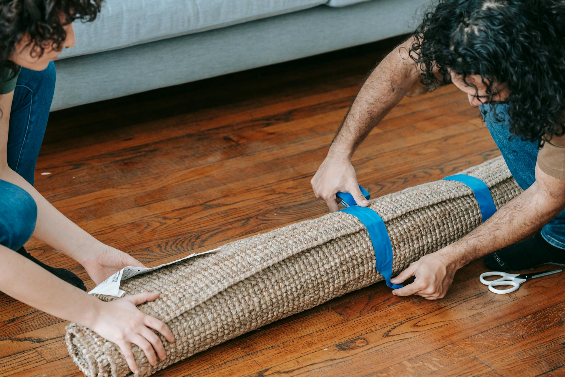 A couple wrapping a rolled carpet with adhesive tape, ready for moving.