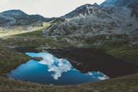 山间湖泊风景优美，倒映着多云的天空，四周环绕着岩石地形和郁郁葱葱的绿植