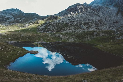 山间湖泊风景优美，倒映着多云的天空，四周环绕着岩石地形和郁郁葱葱的绿植