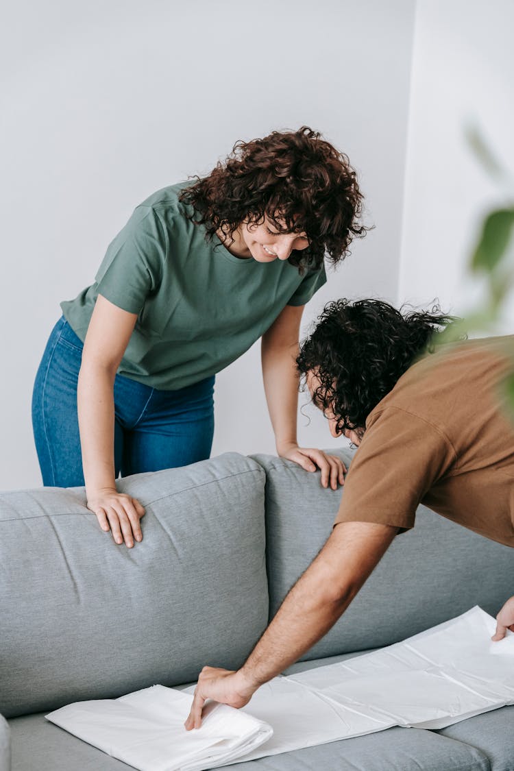 A Couple Putting Cover On A Gray Couch