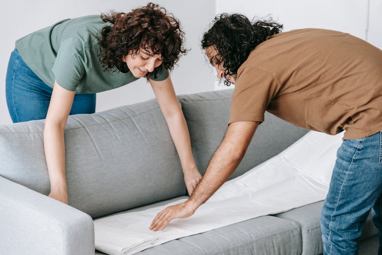 A Couple Putting Cover On A Gray Couch