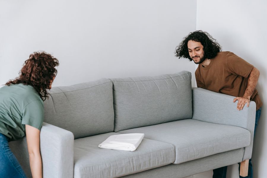 Couple moving a sofa into a bright Dubai living room with a moving crew