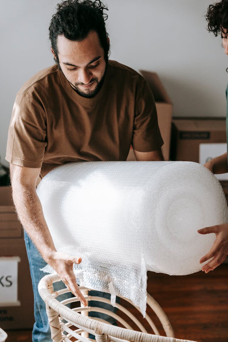 Ethnic Man With Bubble Wrap Near Armchair