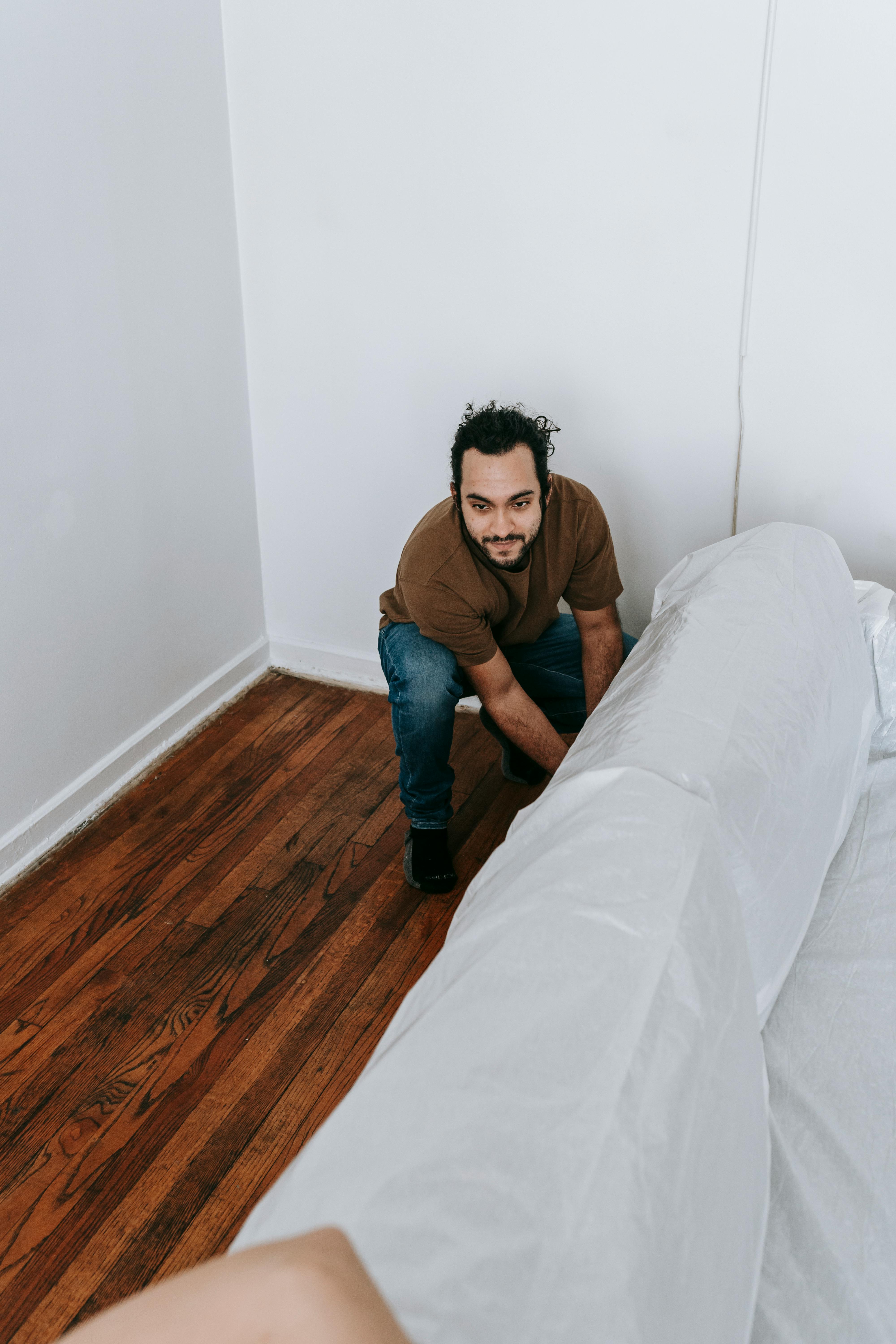 Man covers a sofa with white cloth in a contemporary apartment setting, preparing for relocation.