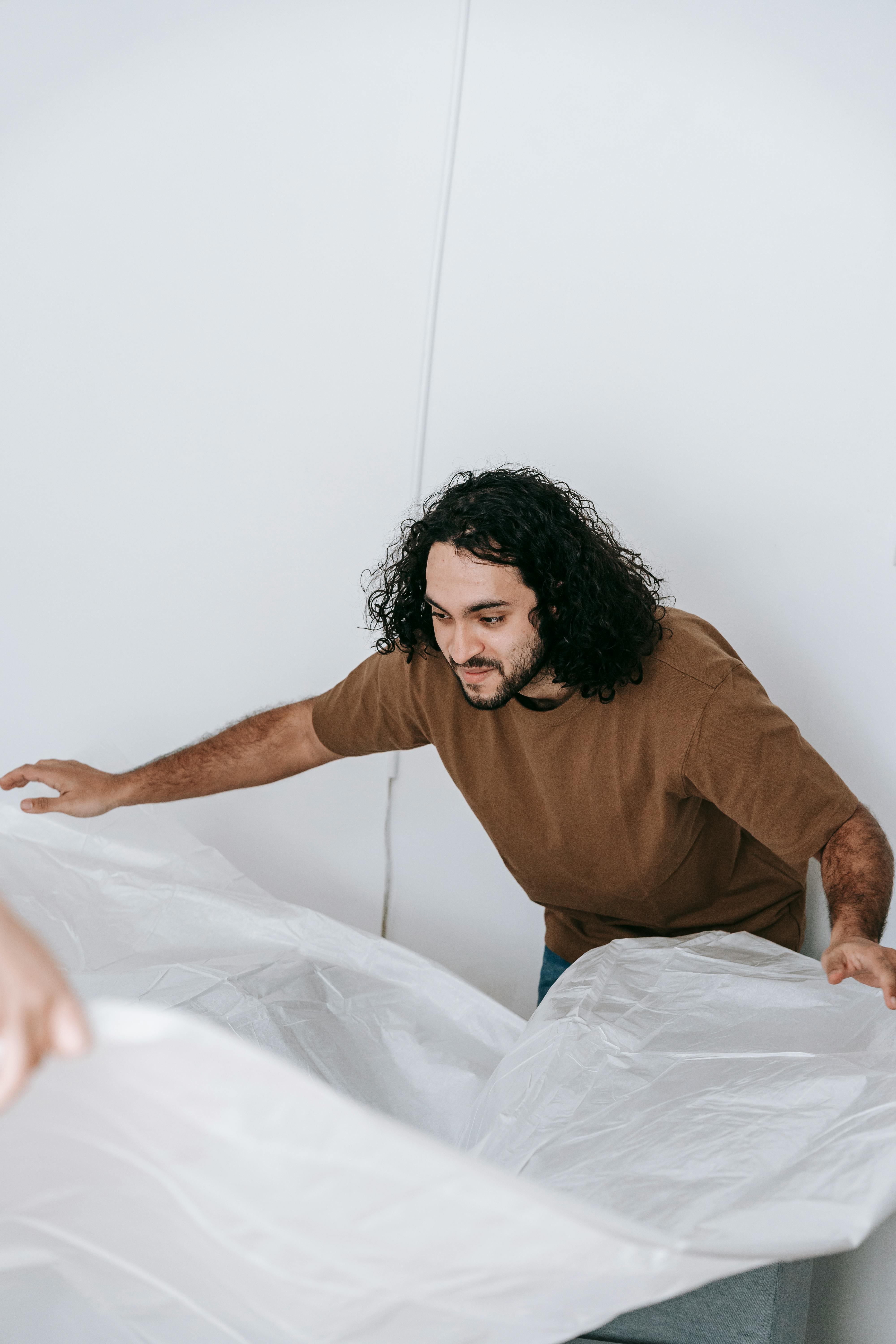 man covering a couch with white cloth