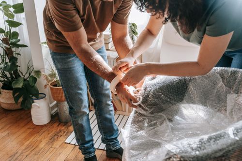 Free A couple wraps furniture with bubble wrap in a sunlit living room, preparing to move. Stock Photo
