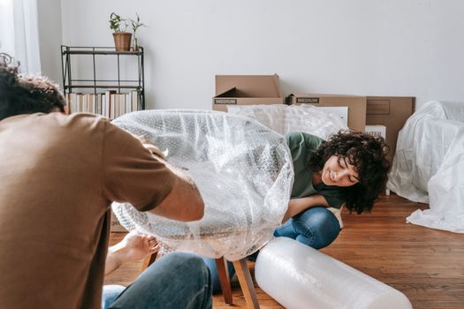 A couple carefully packing chairs with bubble wrap in a sunlit room during a move.