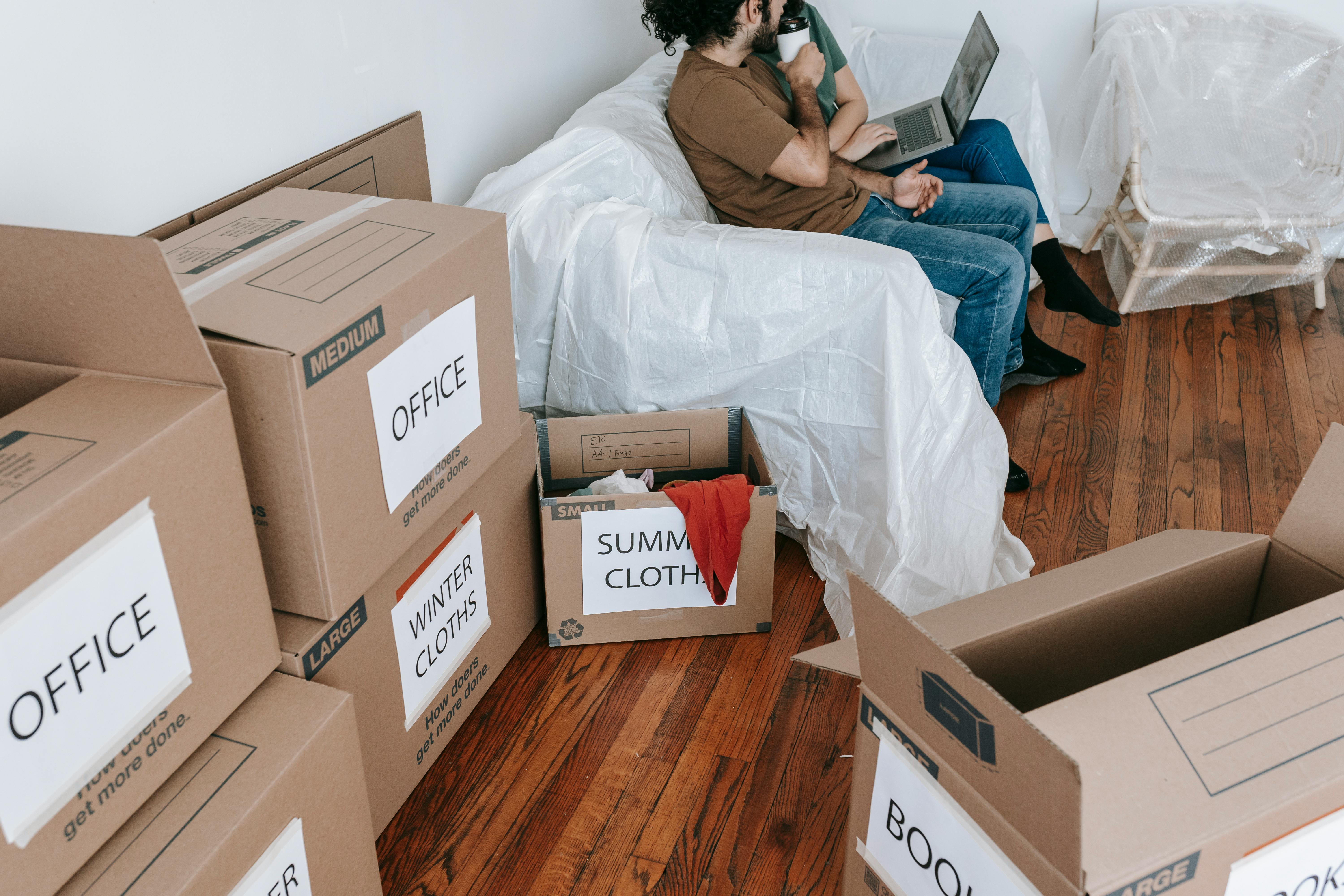 Person Looking Worried While Sitting On A Couch With Moving Boxes In The Background