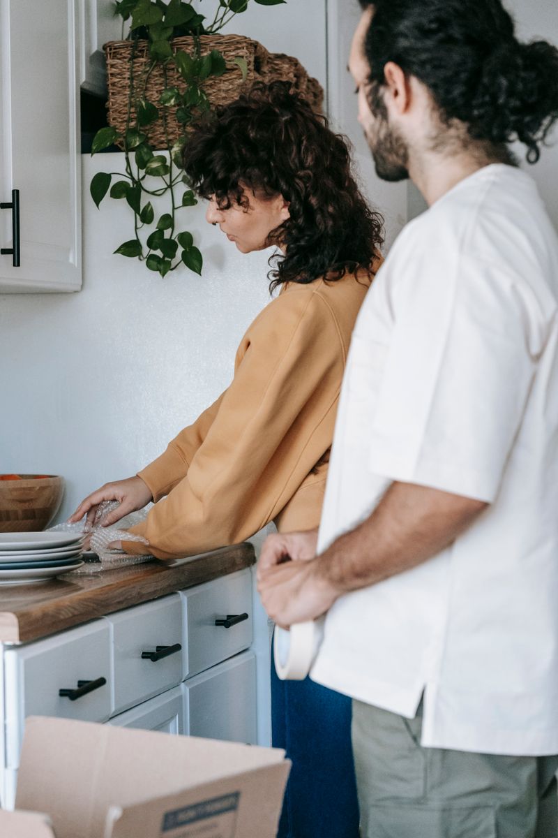 Two adults packing dishes in a modern kitchen, preparing for moving day.