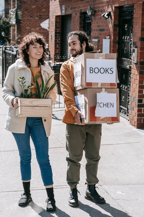 Couple Moving Out Carrying Boxes And Plants