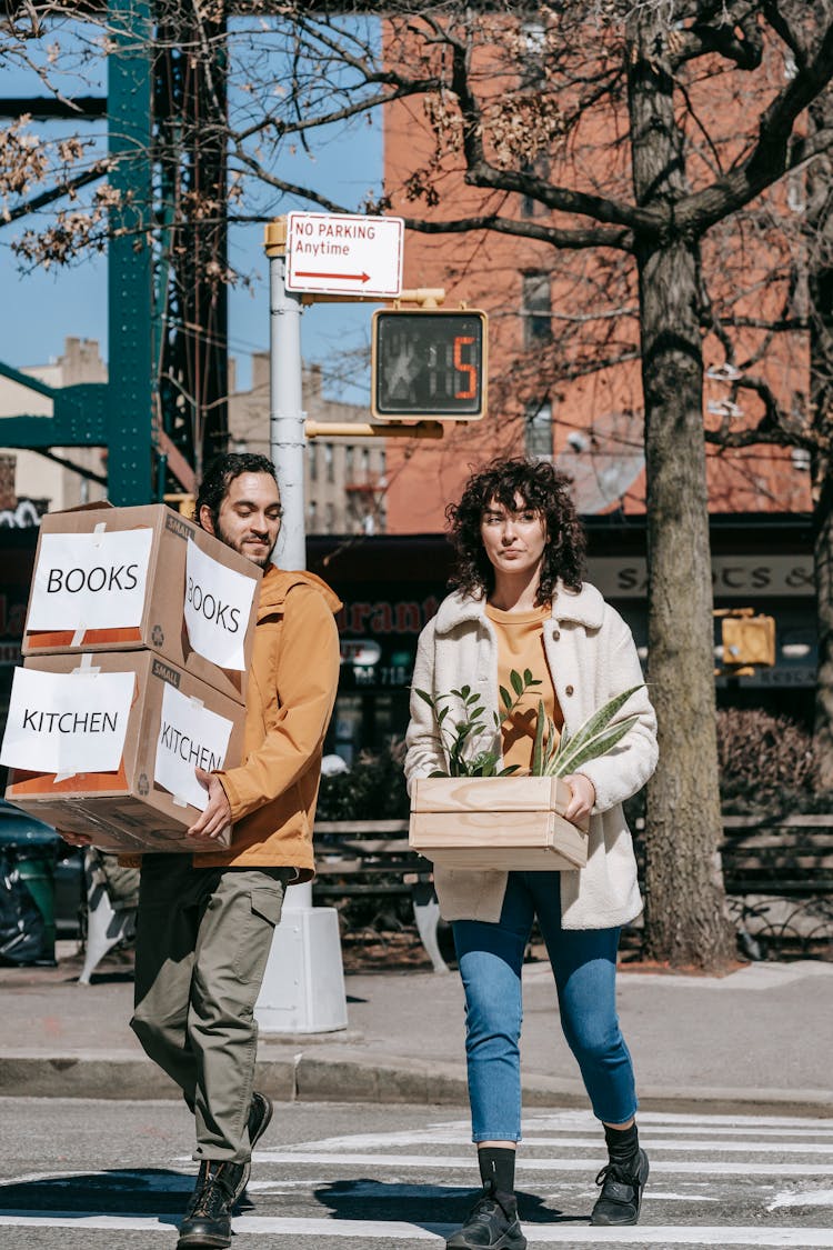 Couple Moving Out Carrying Boxes And Plants