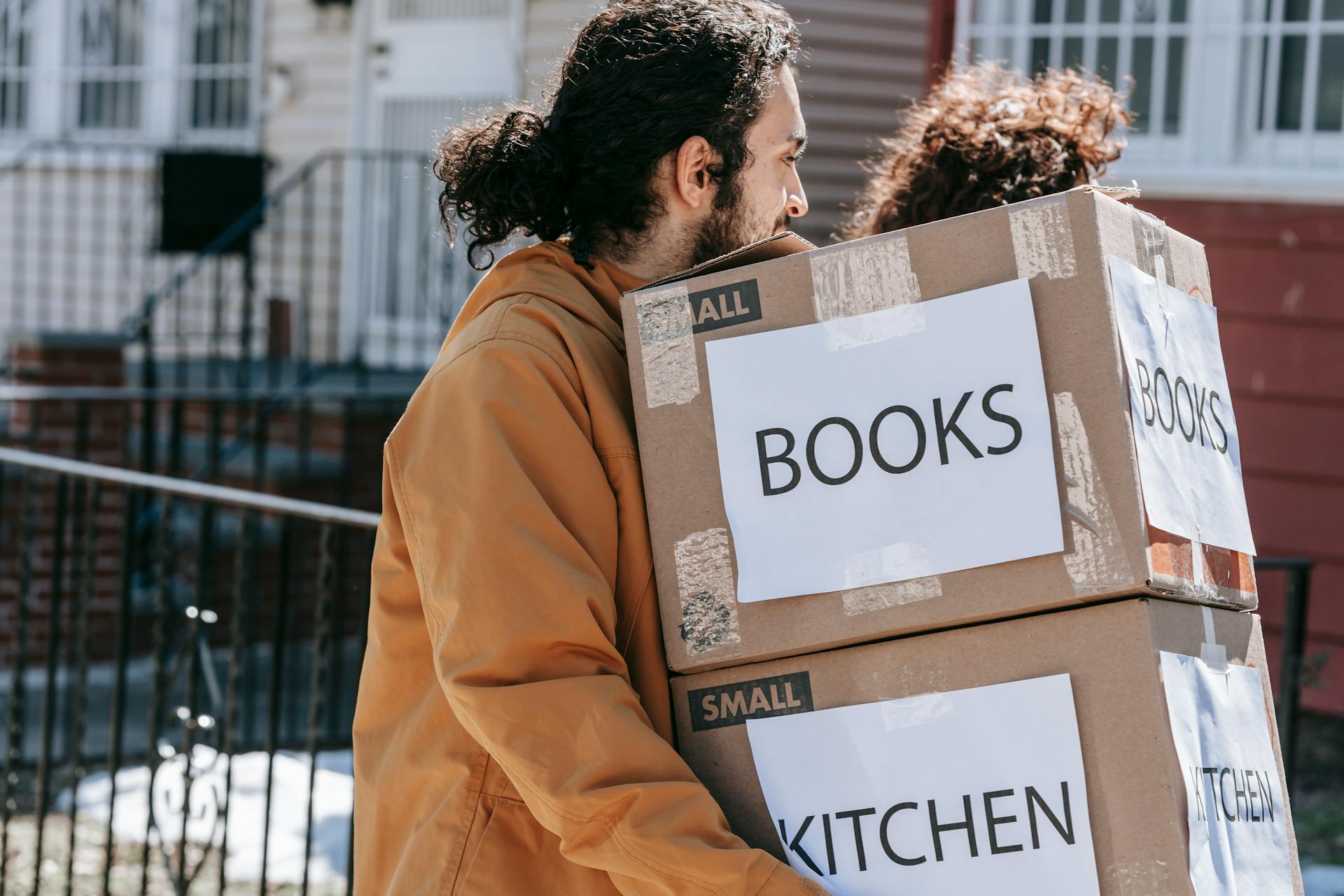 A couple carrying labeled boxes outside, symbolizing moving to a new home.