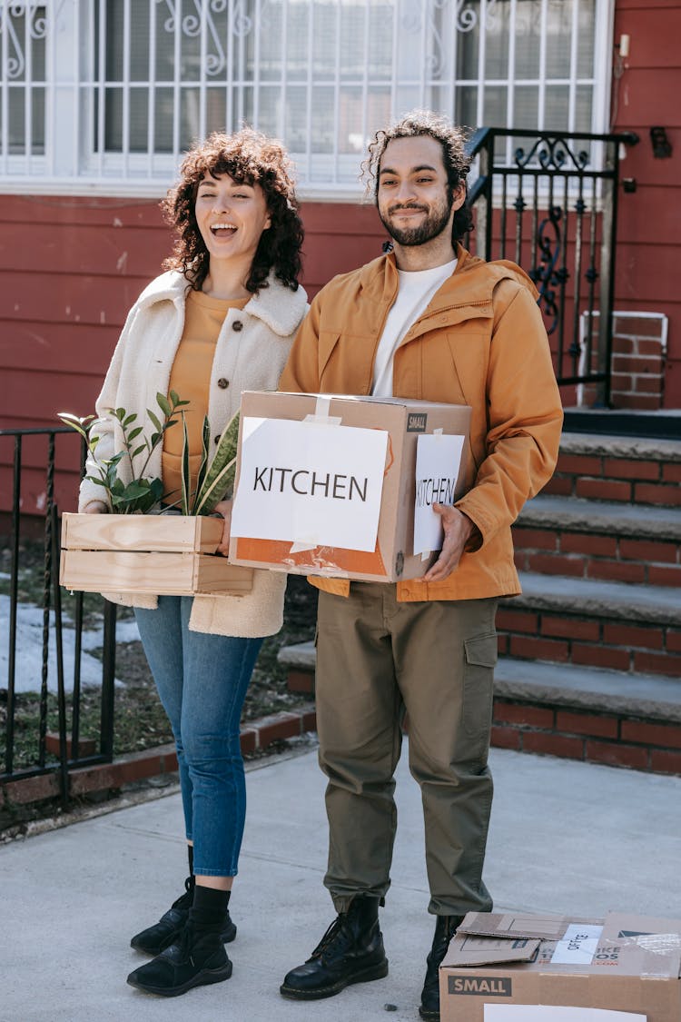 Couple Moving Out Carrying Box And Plants