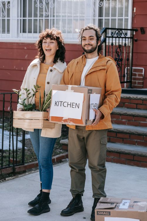 Free Happy couple smiling while carrying boxes into their new home, symbolizing relocation and new beginnings. Stock Photo