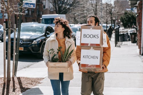 Free Couple Walking On Sidewalk Carrying Boxes And Plants Stock Photo