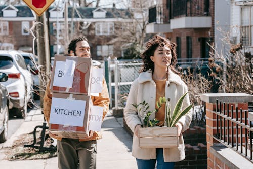 A Couple Moving Out Carrying Boxes And Plants