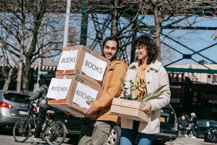 A Couple Moving Out Carrying Boxes And Plants