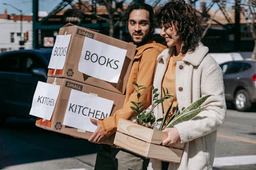 Free Man Carrying Boxes And Woman Holding A Box Of Plants Stock Photo