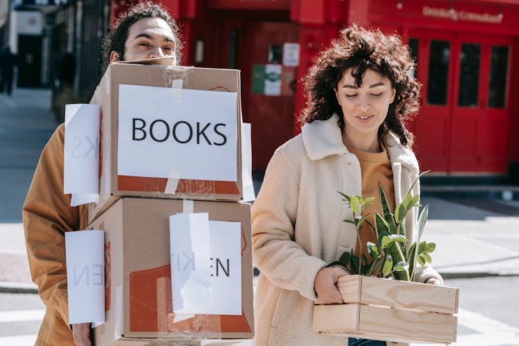 A Couple Carrying Boxes And Plants