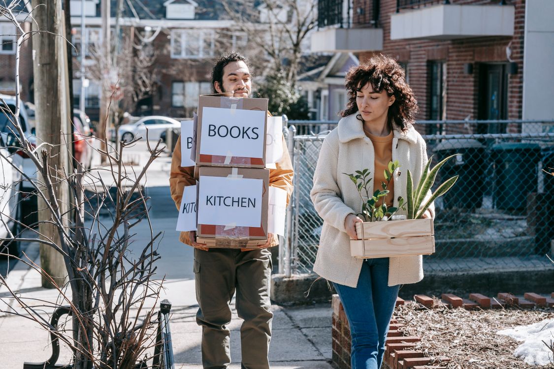 Couple carrying moving boxes and plants into a new apartment