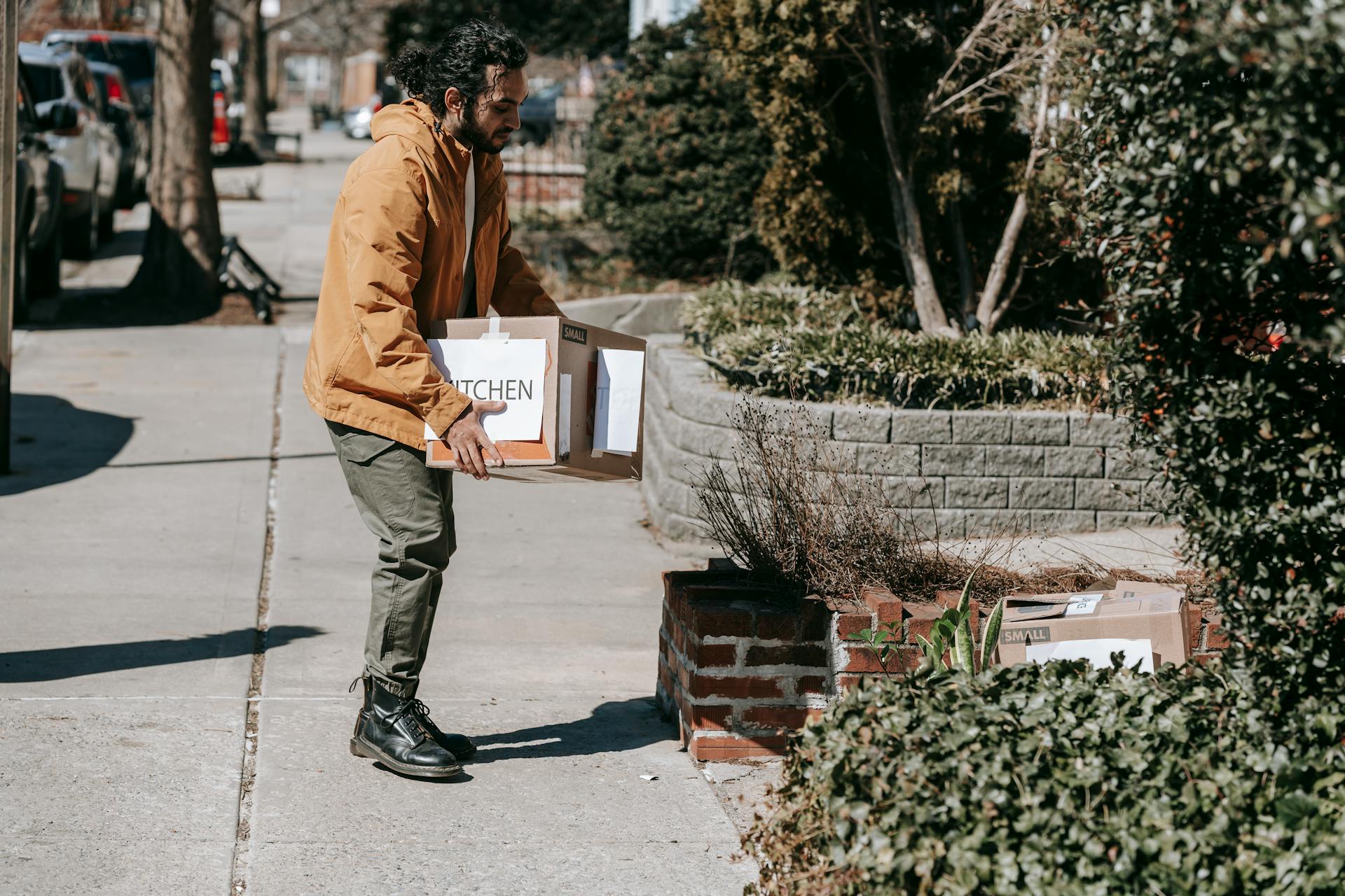 Man carrying boxes on a sunny day, relocating in urban neighborhood.