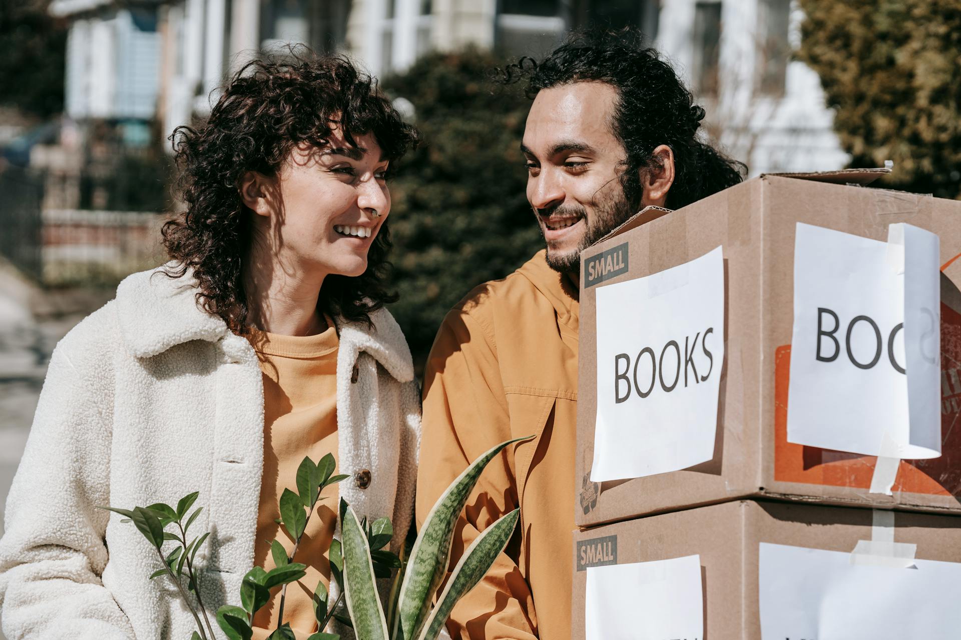 A cheerful couple moving into their new home with boxes and plants on a sunny day.