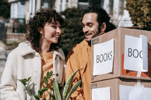 Free A cheerful couple moving into their new home with boxes and plants on a sunny day. Stock Photo