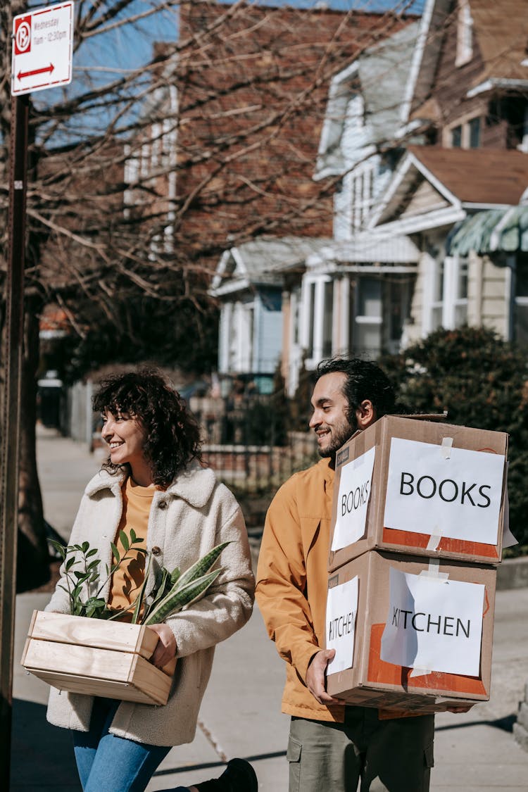 A Couple Moving Out Carrying Plants And Boxes