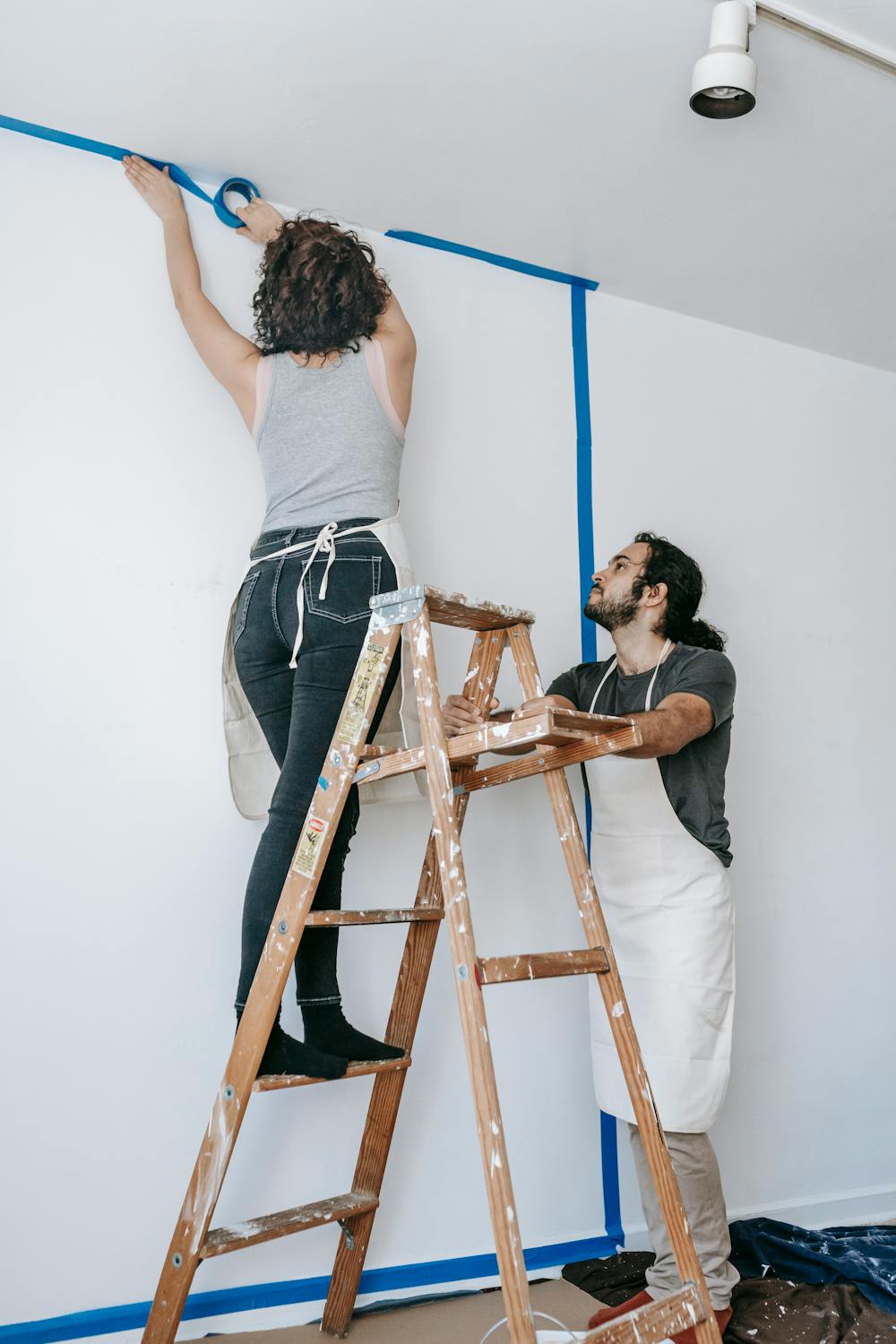 Woman Putting Tape On Wall While The Man Is Holding The Stepladder ...