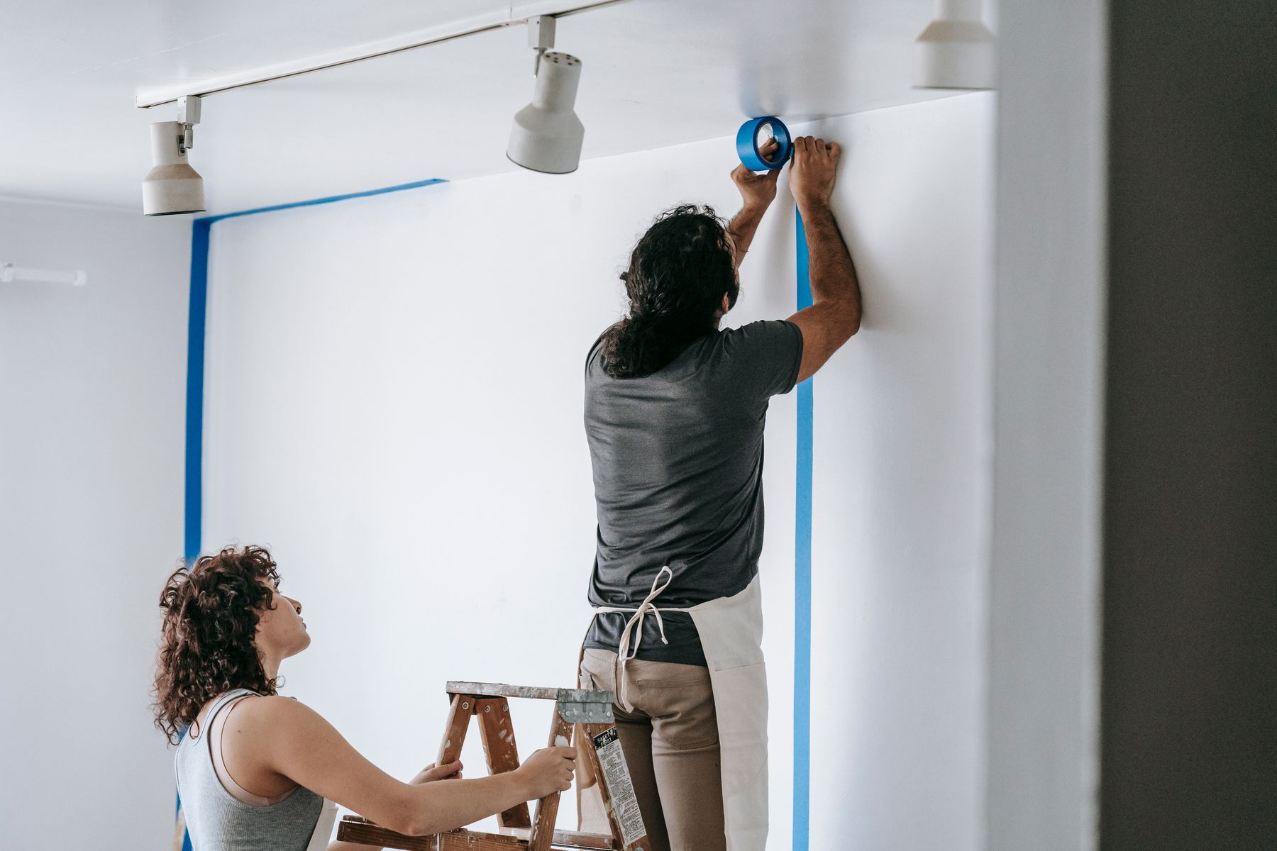 A homeowner and crew member taping a wall together before paint.