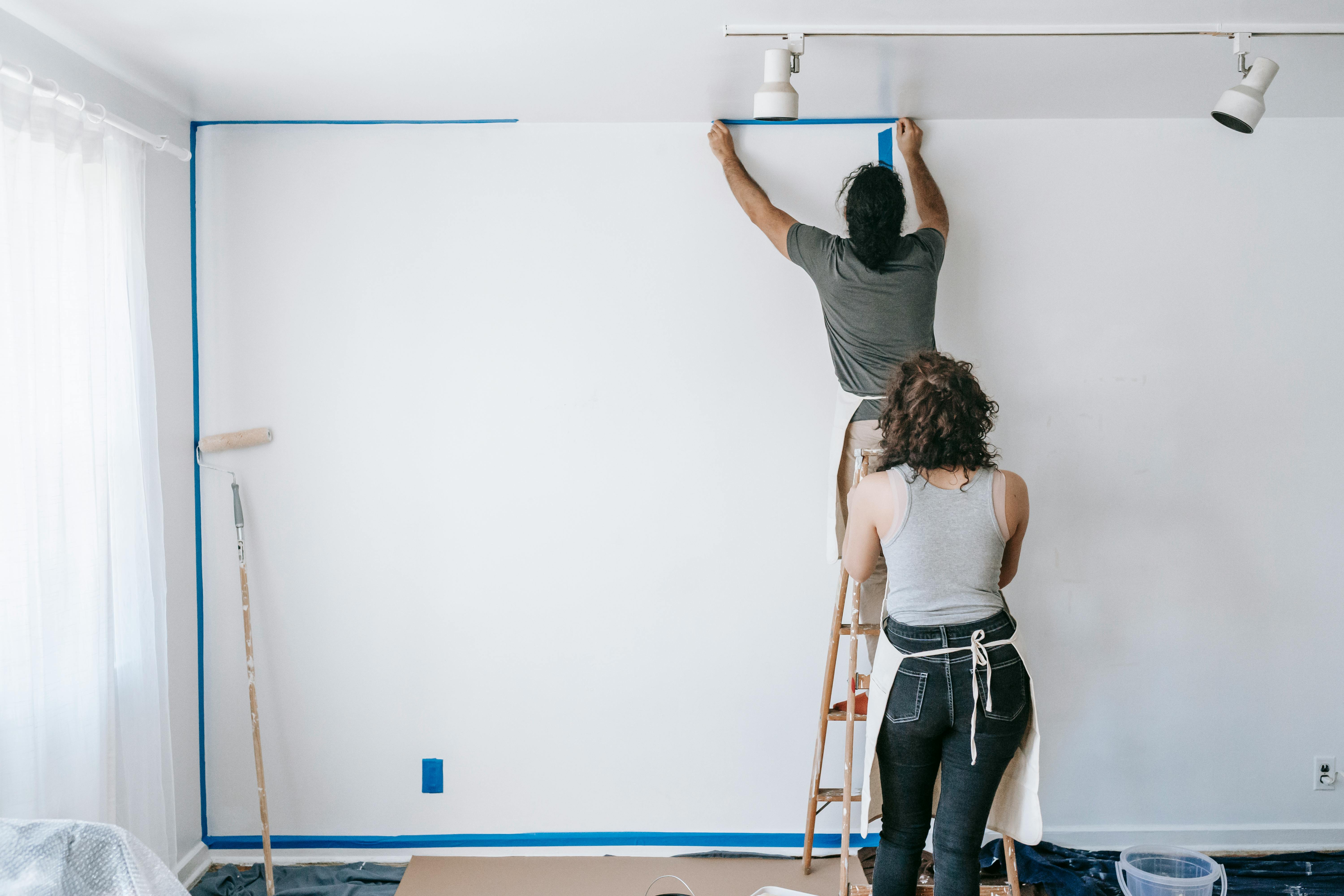 man standing on a stepladder putting tape on wall