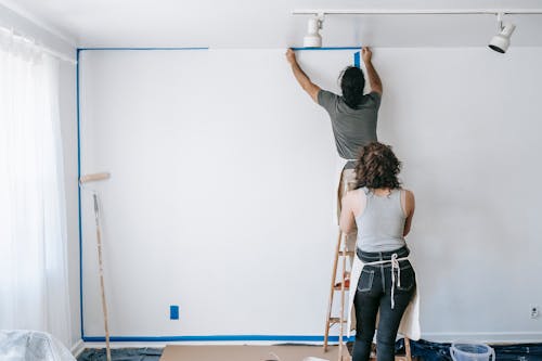 Man Standing On A Stepladder Putting Tape On Wall