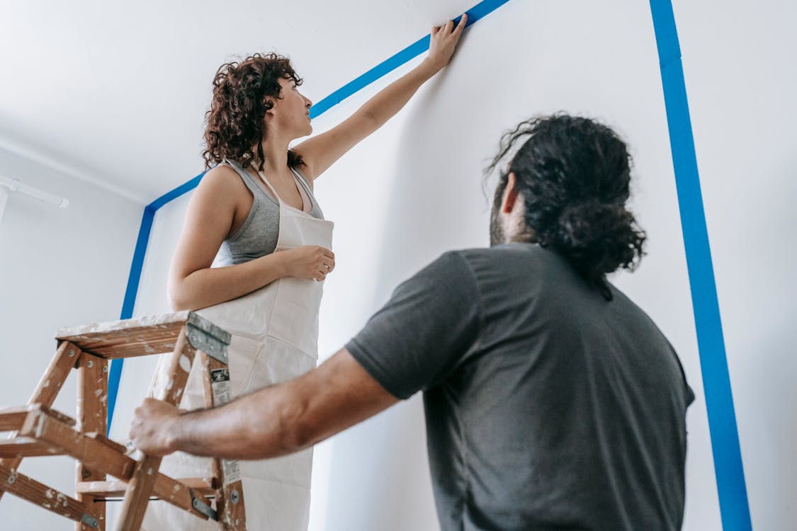 Free Man Standing Beside Woman On A Stepladder Painting The Wall Stock Photo