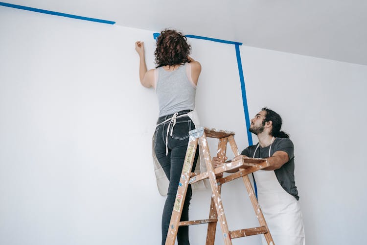 Woman On A Stepladder Painting A Wall