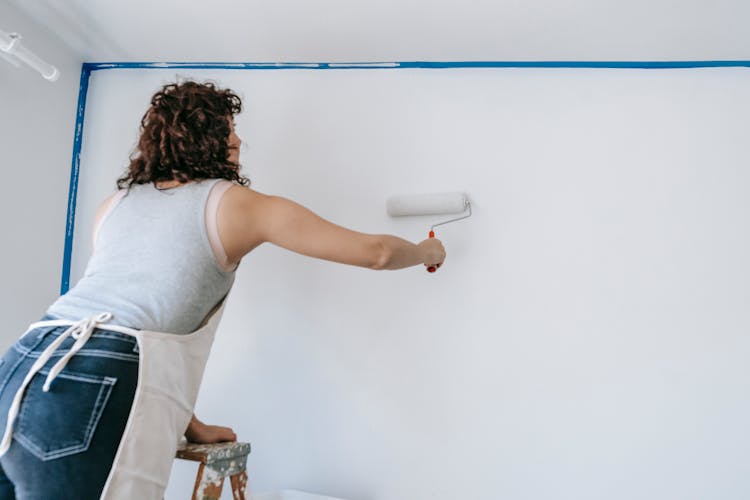 Woman On A Ladder Painting A Wall 