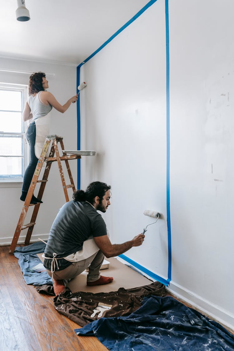 A Couple Painting The Wall Of Their House