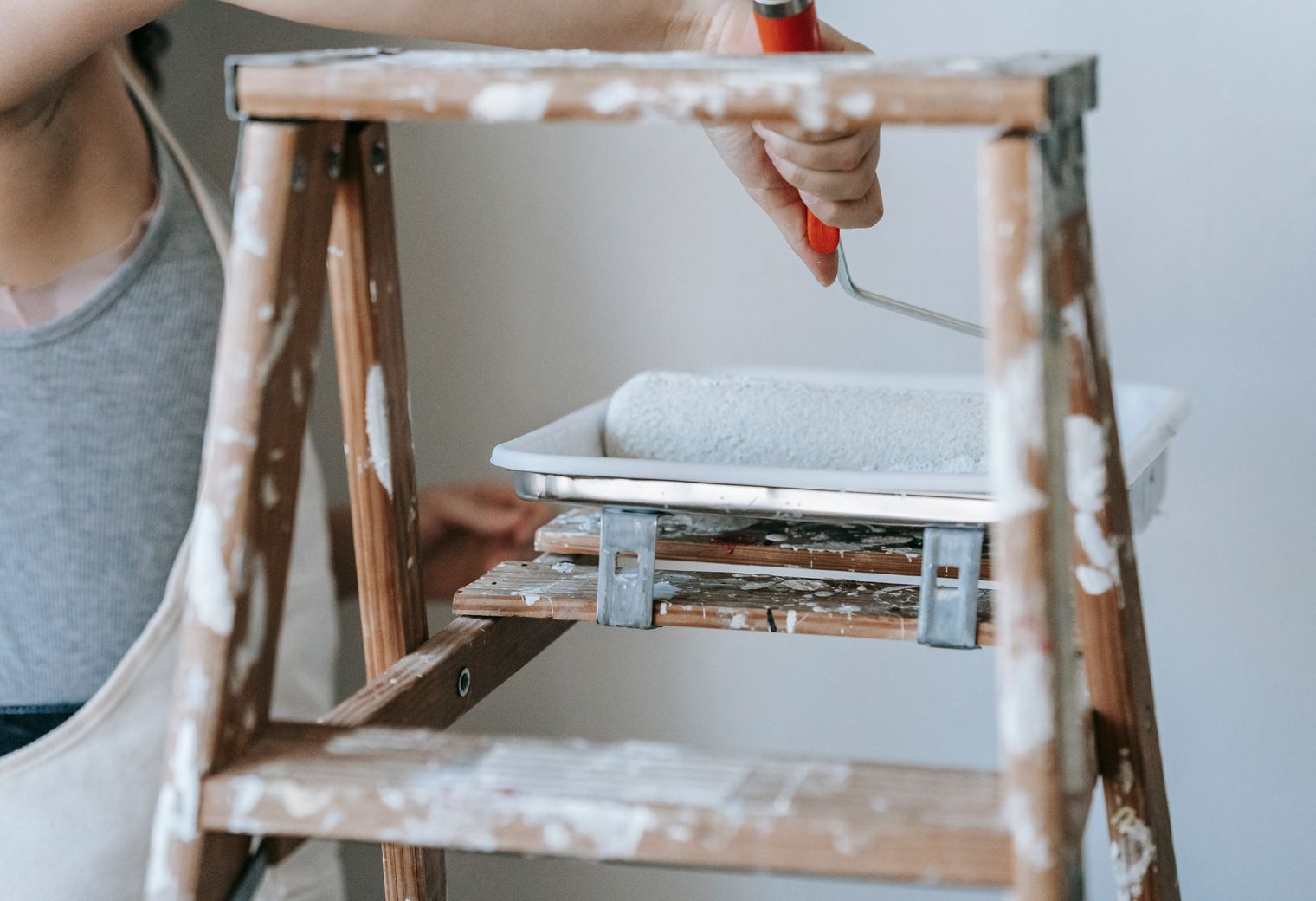 Decorator on a stepladder painting a room wall with a roller
