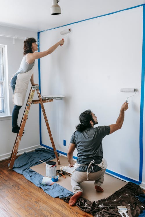 Free A couple collaborates on painting a white wall in their new home, demonstrating teamwork and renovation. Stock Photo