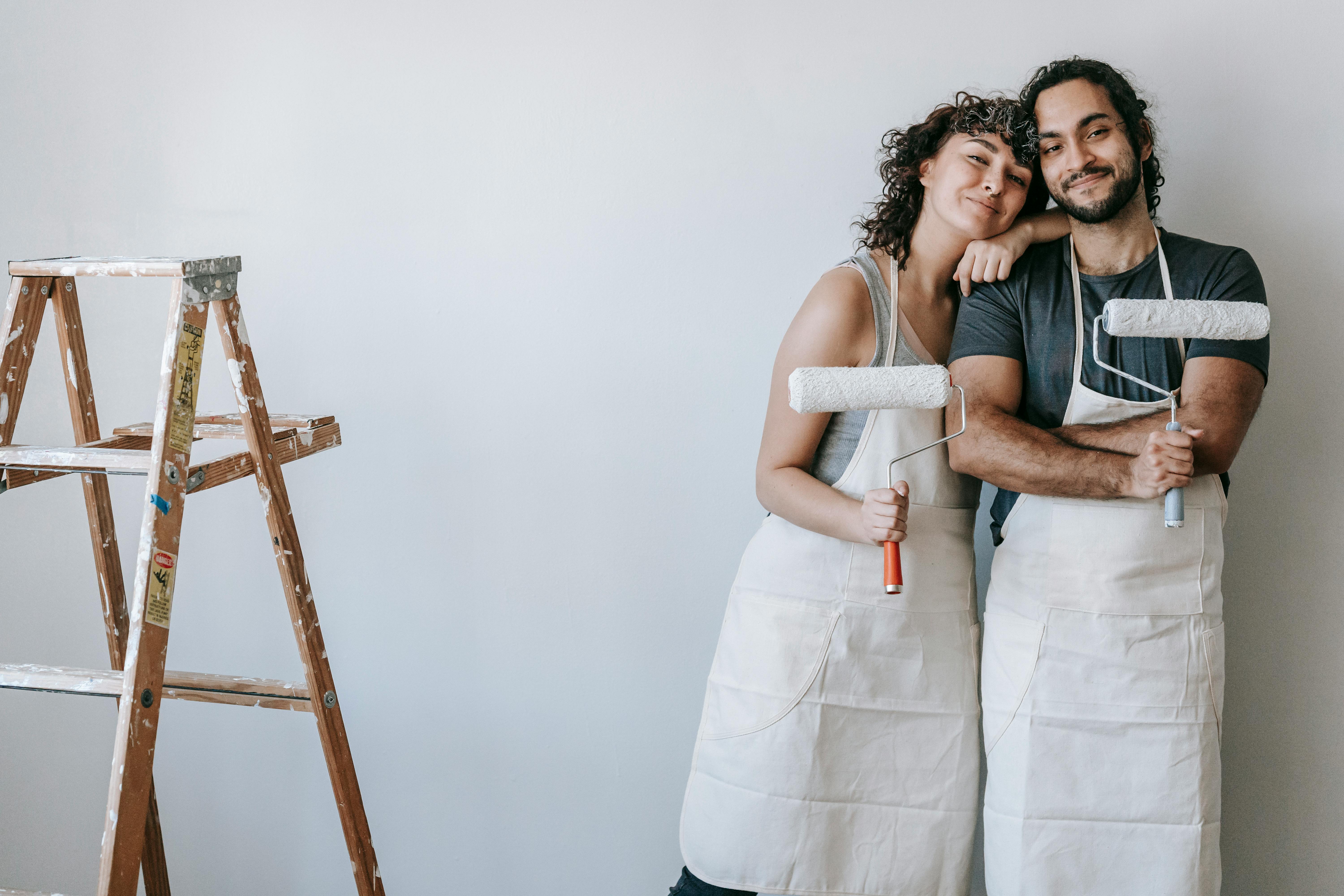 Couple smiling while holding paint rollers during home renovation project.